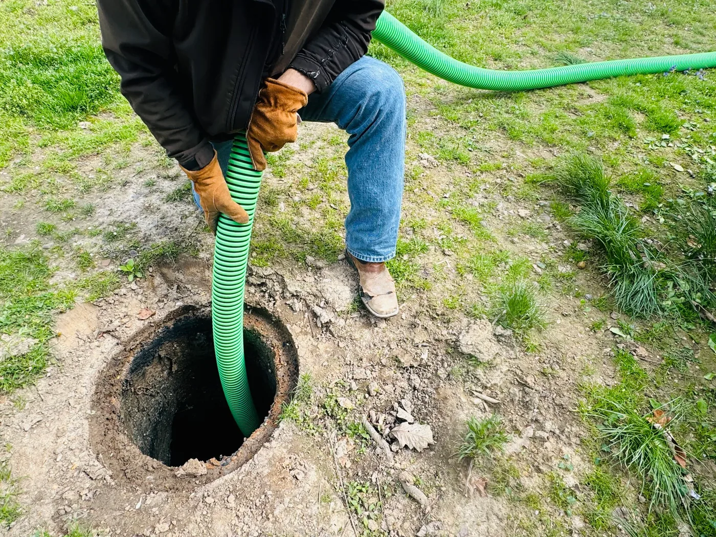 Septic pumping hose being lowered into an open residential septic tank for pump out
