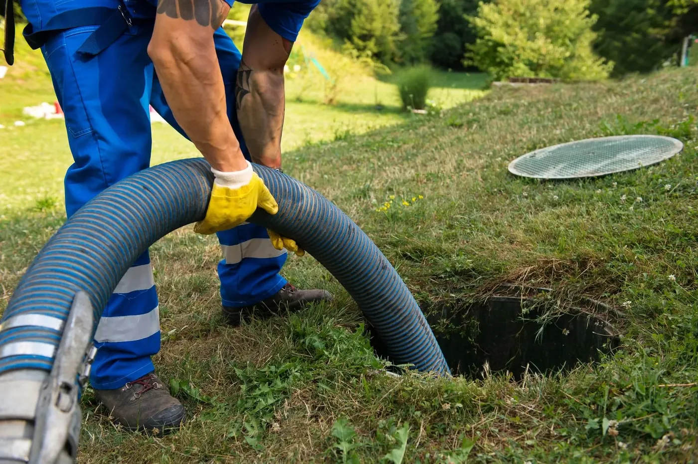 Septic technician operating a thick gray vacuum hose during a thorough septic tank cleaning